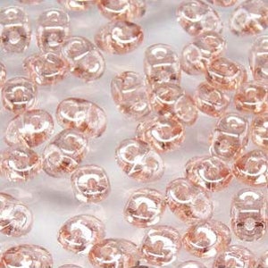 May include: A close-up of a pile of small, clear, pink glass beads. The beads are faceted and have a slightly iridescent finish.