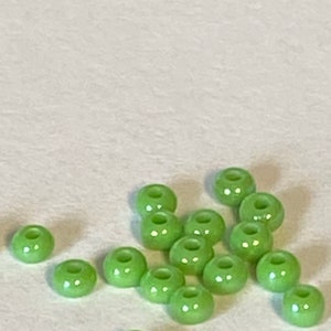 May include: A group of light green glass beads, scattered on a white surface.
