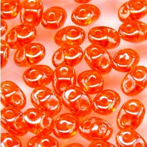 May include: A group of small, orange glass beads with a hole in the center. The beads are oval shaped and have a slightly irregular surface.