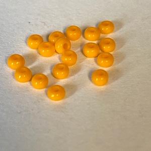 May include: A group of small, round, yellow beads. The beads are scattered on a white surface.