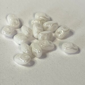 May include: A group of white, pearlescent, oval-shaped beads. The beads have a smooth, glossy finish.