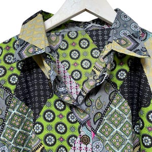 Pu&ograve; includere: Una camicia patchwork colorata con colletto button-down. La camicia presenta una variet&agrave; di motivi, tra cui paisley, floreali e geometrici, nelle tonalit&agrave; di verde, nero, grigio e giallo. La camicia &egrave; appesa a una gruccia bianca.