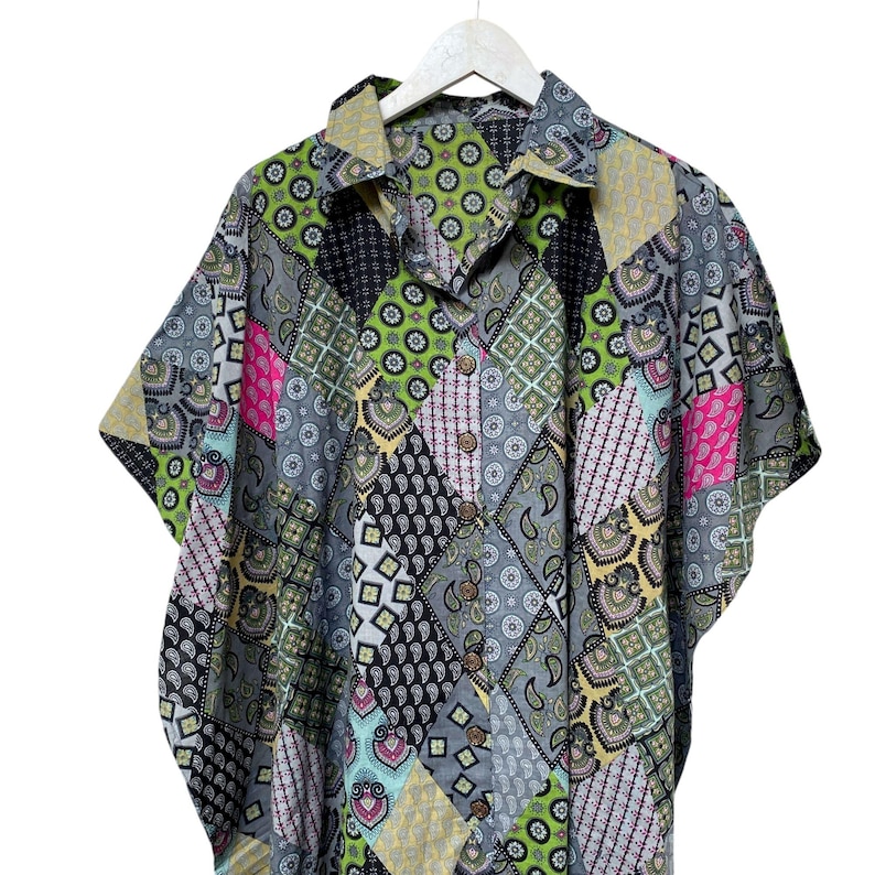 Pu&ograve; includere: Una camicia a maniche corte con un design patchwork. La camicia presenta una variet&agrave; di motivi nelle tonalit&agrave; di grigio, nero, verde, rosa e giallo. &Egrave; abbottonata e appesa a una gruccia bianca.