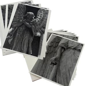 May include: A stack of black and white postcards featuring detailed images of angel statues. The postcards show the statues in various poses, with intricate details of wings, clothing, and facial expressions. The cards have white borders.