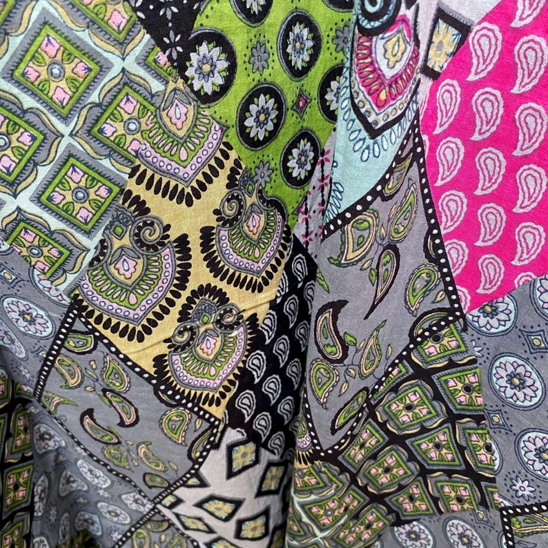 Pu&ograve; includere: Primo piano di un tessuto patchwork con diversi motivi e colori. Il design include motivi paisley, floreali e geometrici in tonalit&agrave; di verde, rosa, grigio, nero e giallo. Il tessuto sembra leggero.