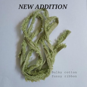 May include: A length of light green, textured ribbon with frayed, fuzzy edges. The text NEW ADDITION appears at the top, and the text Bulky cotton fuzzy ribbon appears at the bottom right of the image, describing the coiled, light green ribbon.