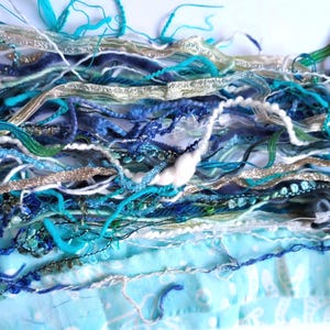 May include: A collection of assorted decorative ribbons and yarns in shades of turquoise, navy blue, light blue, white, and metallic silver. The bundle includes various textures such as velvet, braided cord, shimmering metallic strips, and soft wool.