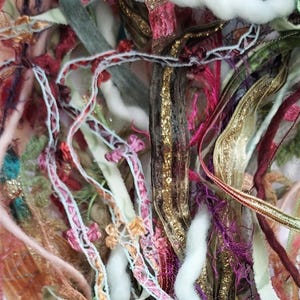 May include: Close-up of a colorful assortment of craft supplies. The image features a mix of ribbons, yarns, and threads in various colors, including gold, pink, purple, and green. The textures vary from smooth to fuzzy, creating a visually rich composition.