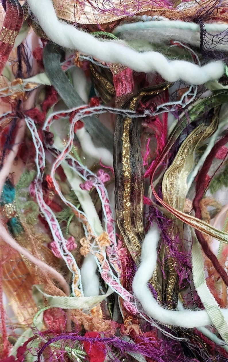 May include: Close-up of a colorful assortment of craft supplies. The image features a mix of ribbons, yarns, and threads in various colors, including gold, pink, purple, and green. The textures vary from smooth to fuzzy, creating a visually rich composition.