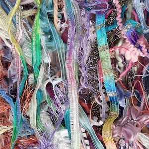 May include: A collection of assorted decorative ribbons and trims in a vibrant array of colors including teal, purple, pink, yellow, and metallic gold. The textures vary from smooth satin and sheer organza to fringed, ruffled, and fuzzy yarn strands.