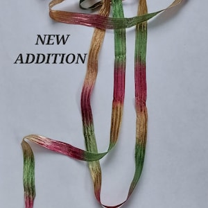 May include: A length of ribbon featuring a gradient color pattern of green, pink, and gold. The ribbon has a textured, woven appearance. The text NEW ADDITION is printed in black on the left side of the image, next to the ribbon strands.