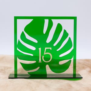 May include: Green acrylic table number with a cutout of a monstera leaf and the number 15 in gold.