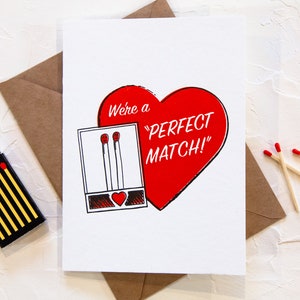 May include: A white card with a red heart that says "We're a "PERFECT MATCH!" with a black and white illustration of a matchbook with two matches inside.