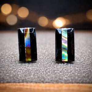 May include: Two rectangular black cufflinks with a vertical iridescent stripe. The stripe features a blend of colors including blue, green, and gold. The cufflinks are displayed on a textured surface.