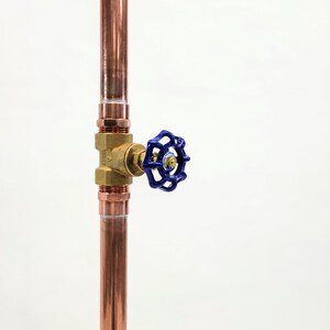 Puede incluir: Tubo de cobre vertical con racor de lat&oacute;n y v&aacute;lvula azul. La v&aacute;lvula tiene un mango azul. El tubo est&aacute; sobre un fondo blanco. Componente de fontaner&iacute;a.