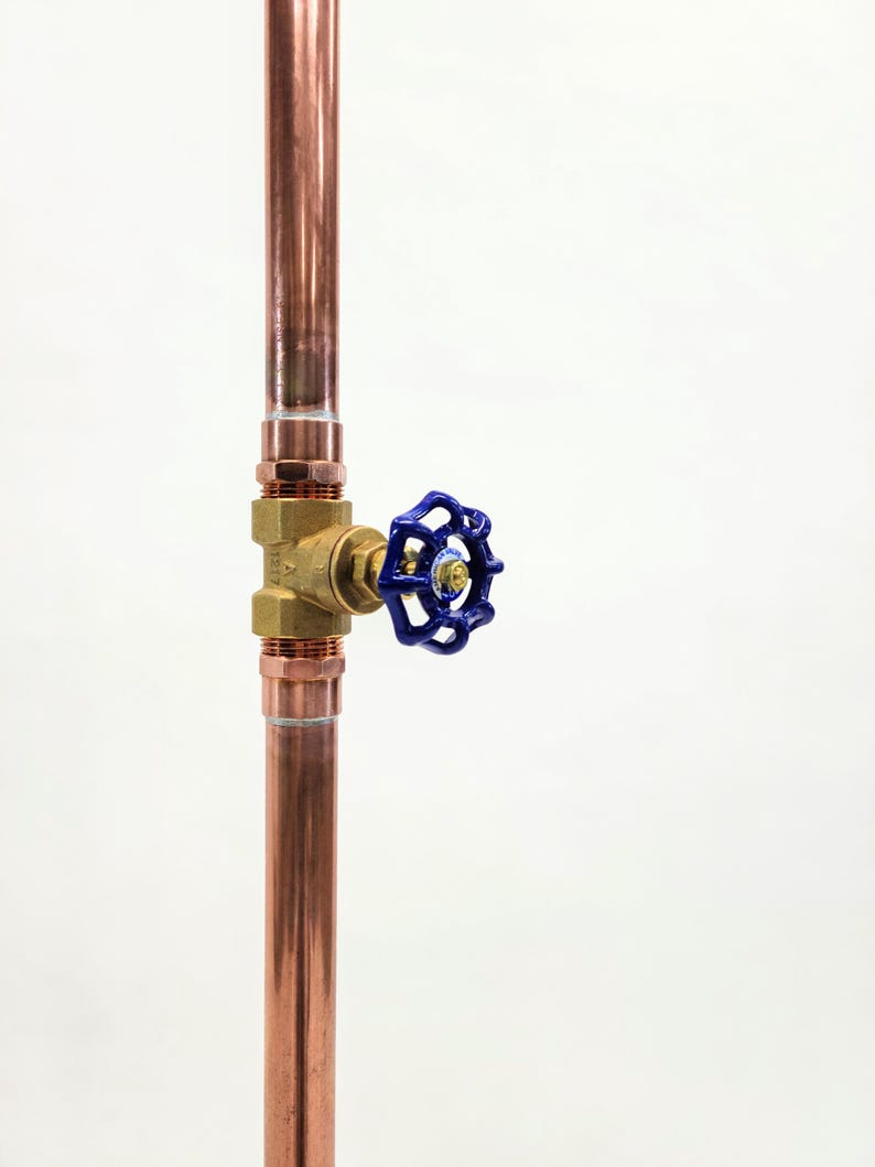 Puede incluir: Tubo de cobre vertical con racor de lat&oacute;n y v&aacute;lvula azul. La v&aacute;lvula tiene un mango azul. El tubo est&aacute; sobre un fondo blanco. Componente de fontaner&iacute;a.