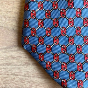 May include: A blue silk tie with a repeating pattern of red circles connected by a white rope design.