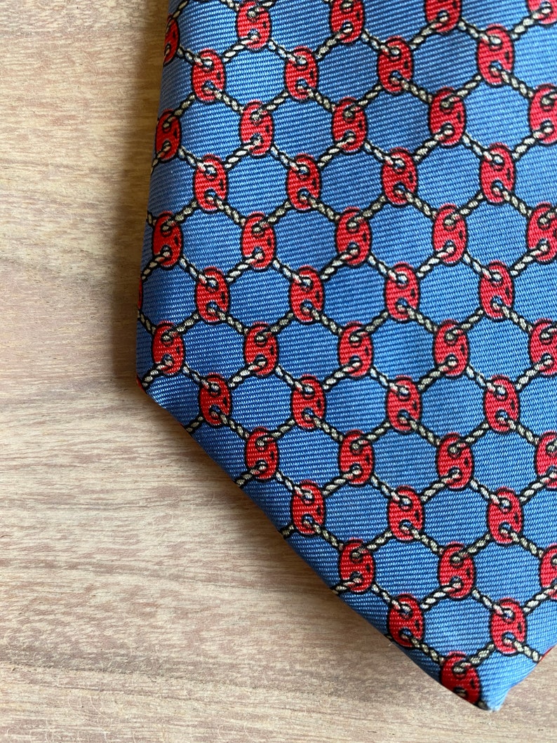 May include: A blue silk tie with a repeating pattern of red circles connected by a white rope design.