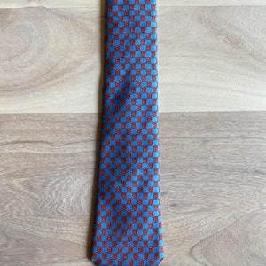 May include: A blue silk tie with a red and white geometric pattern.