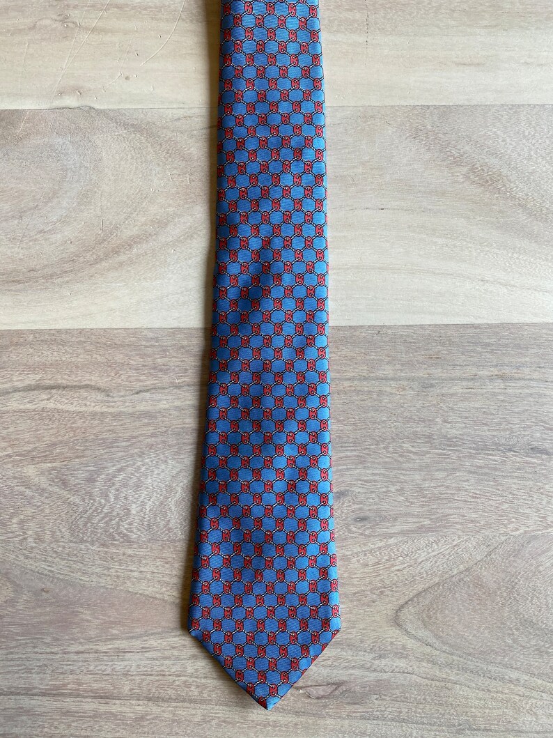 May include: A blue silk tie with a red and white geometric pattern.