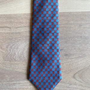 May include: A blue silk tie with a repeating pattern of red interlocking circles.