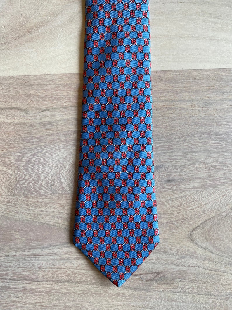May include: A blue silk tie with a repeating pattern of red interlocking circles.
