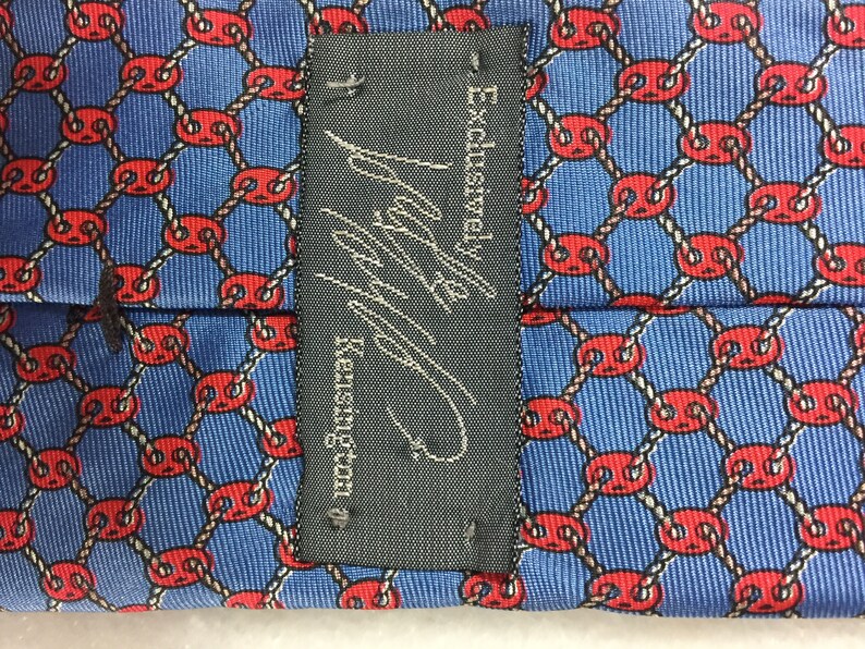 May include: A black tie with a white label that reads "Exclusive!  Navy & Kensington". The tie has a blue background with a repeating pattern of red circles connected by white rope.
