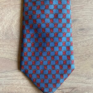May include: A blue silk tie with a red and white geometric pattern. The pattern is a repeating design of interlocking circles.
