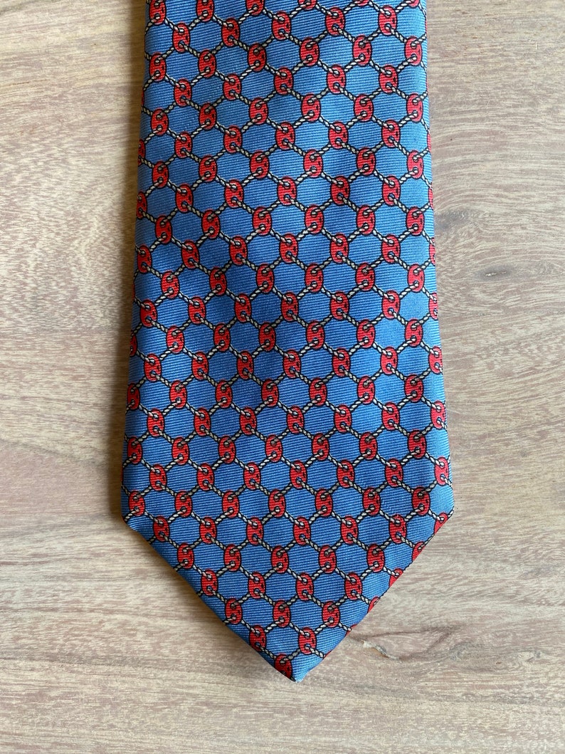 May include: A blue silk tie with a red and white geometric pattern. The pattern is a repeating design of interlocking circles.