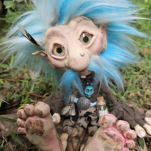 Könnte beinhalten: Eine blaue Trollpuppe mit langem weißem Bart, die ein braunes und schwarzes Outfit trägt und auf einem Blätterbett sitzt. Die Puppe hat eine kleine Flasche mit einem Totenkopf- und Knochen-Etikett an ihrem Gürtel.