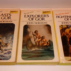 May include: Three mass market paperback books from the Gor series by John Norman, titled Beasts of Gor, Explorers of Gor, and Fighting Slave of Gor. Each book cover features a colorful fantasy illustration, white borders, and yellow edges.