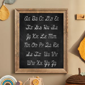 May include: A framed chalkboard with a wooden frame, displaying the alphabet in cursive handwriting. The letters are written in white on a black background.