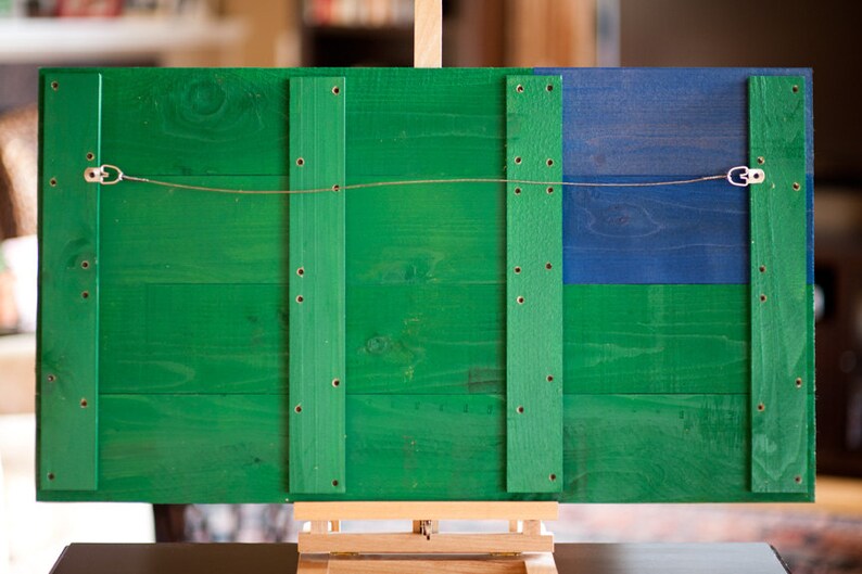 May include: A wooden sign with a green and blue paint finish. The sign has four vertical wooden strips with screws and a wire hanger attached to the top.