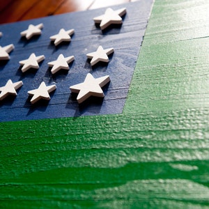 May include: A wooden flag with a blue background and a green stripe. The flag has white stars on the blue background.