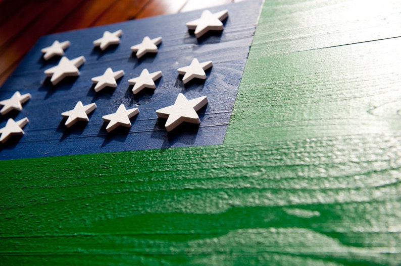 May include: A wooden flag with a blue background and a green stripe. The flag has white stars on the blue background.