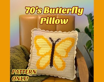 Op de afbeelding: Een gehaakt kussen met een geel vlinderontwerp. Het kussen heeft een gegolfde rand en ligt op een bruine stoel. De tekst "70's Butterfly Pillow" en "PATTERN ONLY!" is zichtbaar in de afbeelding.