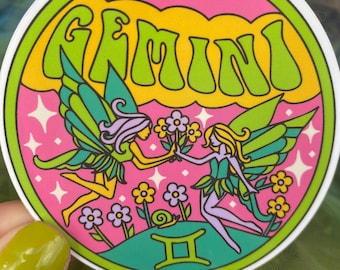 May include: A pink and green circular sticker with the word "GEMINI" in a retro font. The sticker features two fairies with wings, flowers, and a snail. The astrological symbol for Gemini is also included.