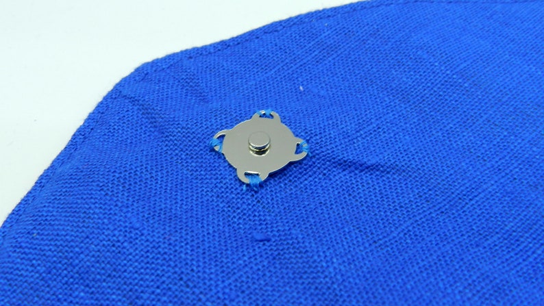May include: A silver magnetic snap closure attached to a piece of bright blue fabric. The snap has a circular center and a decorative, four-lobed outer design. The fabric appears to be a woven material.