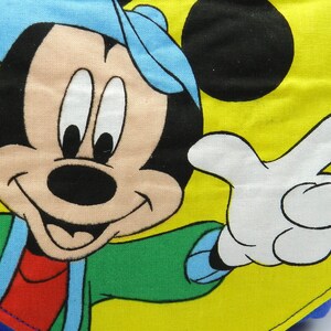 May include: A yellow and blue backpack featuring a large graphic of Mickey Mouse. The cartoon character is wearing a blue hat and green jacket, with a white gloved hand pointing. The backpack has blue straps.