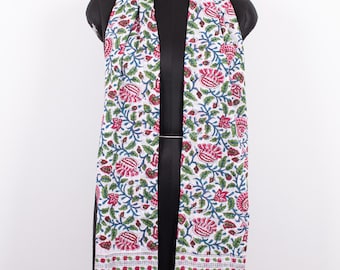 May include: A white scarf featuring a repeating floral pattern in shades of pink, green, and blue. The design includes stylized flowers and leafy vines, with a horizontal border at the bottom consisting of small floral motifs and blue vertical stripes.