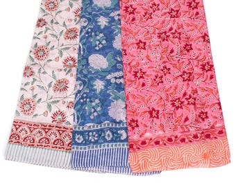 May include: Three rectangular fabric pieces featuring floral block print patterns. The left piece is white with red and green flowers, the center is blue with white floral motifs, and the right is pink with red floral patterns and an orange border.