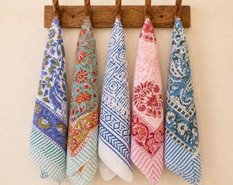May include: Five rectangular cotton napkins hanging from a wooden rack with five hooks. Each napkin features a distinct block-printed pattern in various colors including blue, green, pink, and white, with floral, geometric, and striped motifs.