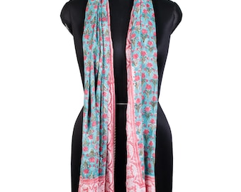 May include: A long rectangular scarf featuring a light blue background with a repeating pattern of small pink floral motifs. The edges of the scarf are bordered by a wider band of pink floral designs and a thin green and white striped hem at the bottom.