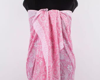 May include: A pink and white sarong featuring a detailed floral and paisley pattern with a chevron border. The fabric is draped over a black mannequin torso, showcasing the intricate botanical motifs and the contrasting light pink and white color palette.