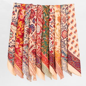 May include: A collection of rectangular fabric pieces hanging side by side, each featuring distinct block-printed floral and geometric patterns in vibrant shades of red, green, yellow, blue, and cream, with decorative borders on the edges.