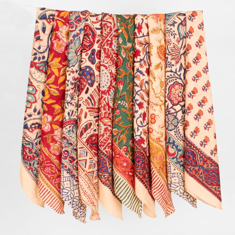 May include: A collection of rectangular fabric pieces hanging side by side, each featuring distinct block-printed floral and geometric patterns in vibrant shades of red, green, yellow, blue, and cream, with decorative borders on the edges.