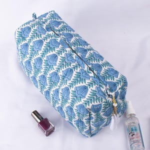 May include: A white quilted makeup bag with a blue floral print. The bag has a zipper closure and a gold tassel.