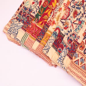 May include: A collection of folded fabric strips featuring a variety of block-printed patterns in shades of red, blue, green, and yellow on a cream-colored background. The designs include floral motifs, geometric shapes, and striped borders.