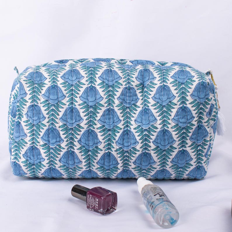 May include: A blue and white quilted makeup bag with a floral pattern. The bag has a zipper closure and a tassel pull.