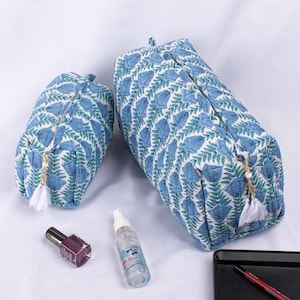 May include: Two blue and white floral print zippered pouches with white tassels. The larger pouch is on the right and the smaller pouch is on the left. The pouches are on a white surface.